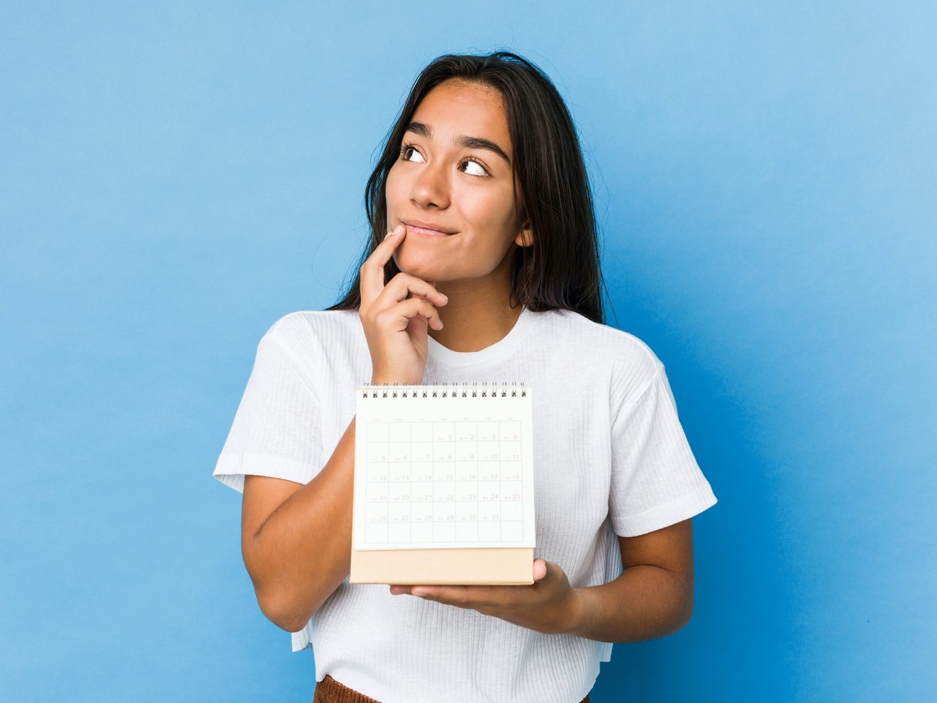 Junge Frau mit nachdenklichem Blick hält einen kleinen Kalender in der Hand