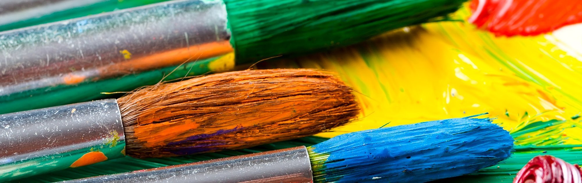 Bunte Pinsel liegen auf einer Palette mit verstrichener Farbe in kräftigen Tönen