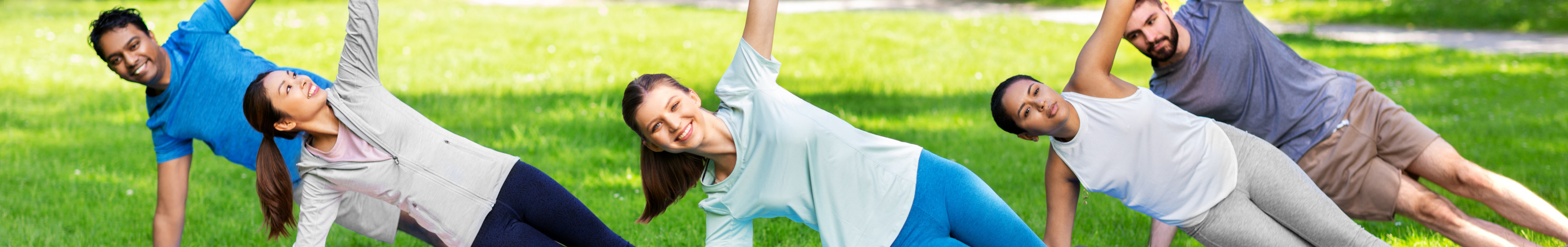 Gruppe von Menschen macht seitliche Plank-Übung im Park auf einer Wiese