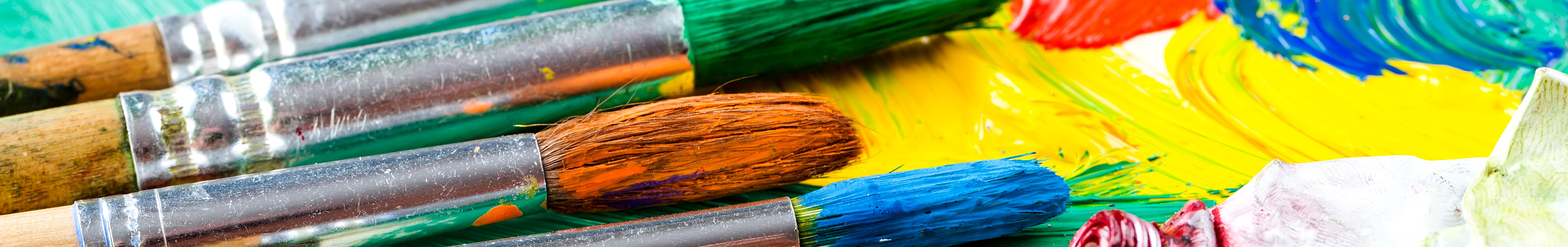 Bunte Pinsel liegen auf einer Palette mit verstrichener Farbe in kräftigen Tönen